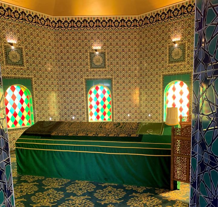 Ornate walls with windows, long green cloth over table.